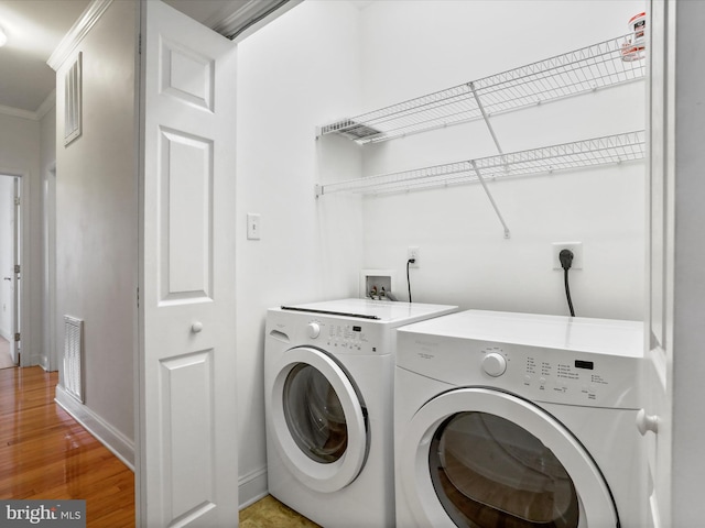 laundry room with washing machine and dryer, ornamental molding, and hardwood / wood-style flooring