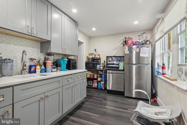 kitchen with decorative backsplash, dark hardwood / wood-style flooring, gray cabinetry, light stone countertops, and stainless steel appliances