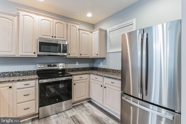 kitchen with stainless steel appliances, light hardwood / wood-style floors, and dark stone countertops