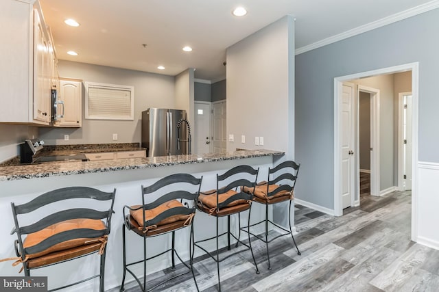 kitchen with light hardwood / wood-style floors, range, kitchen peninsula, stainless steel fridge, and dark stone countertops