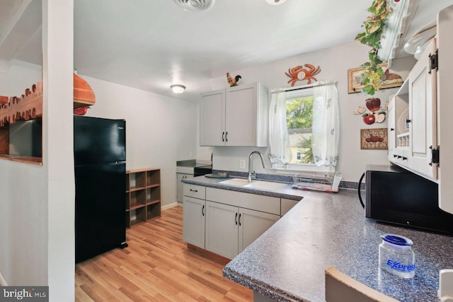 kitchen with visible vents, white cabinets, light wood-style floors, black appliances, and a sink