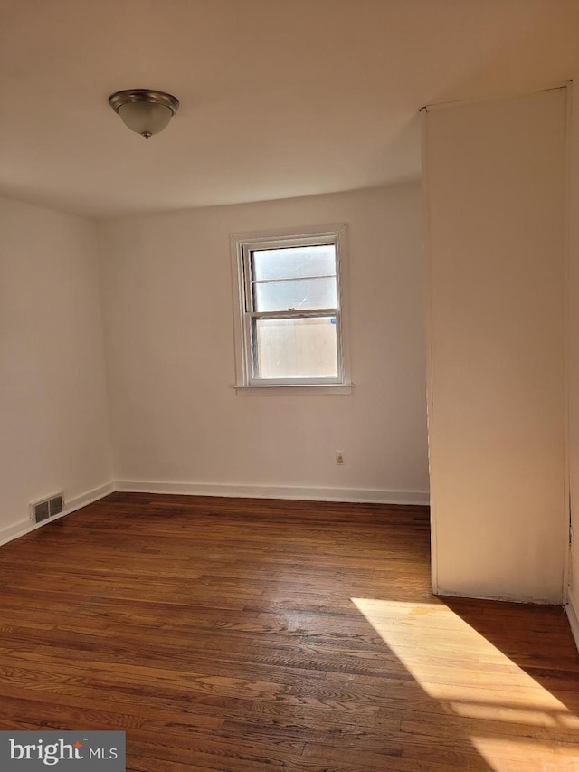 unfurnished room with baseboards, visible vents, and dark wood finished floors