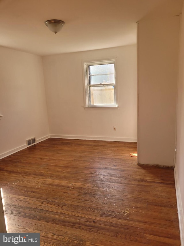 unfurnished room featuring baseboards, visible vents, and dark wood finished floors