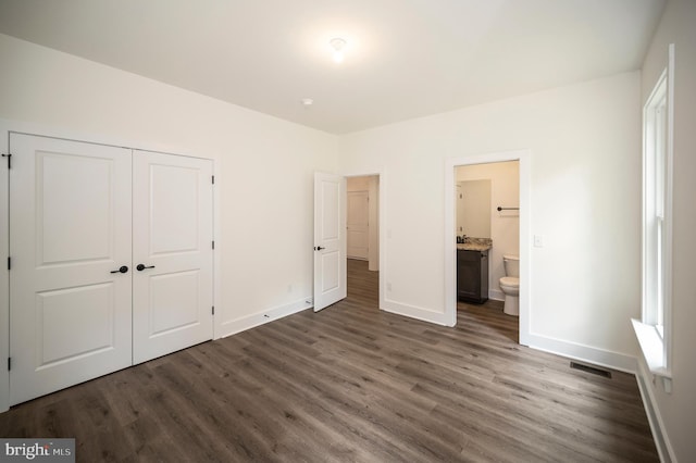 unfurnished bedroom with connected bathroom, a closet, and dark hardwood / wood-style floors