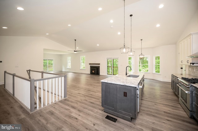 kitchen with sink, white cabinetry, high end range, decorative light fixtures, and a large island with sink