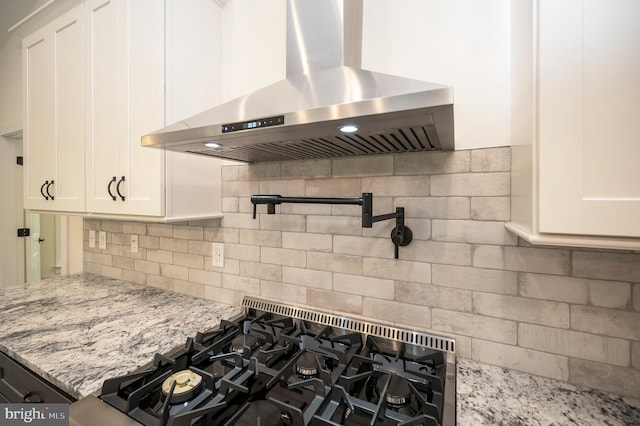 kitchen featuring light stone countertops, tasteful backsplash, wall chimney range hood, and white cabinetry