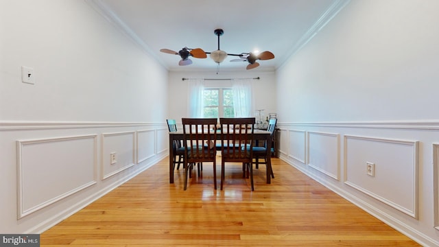 dining area featuring light wood-style flooring, ornamental molding, a decorative wall, and a ceiling fan