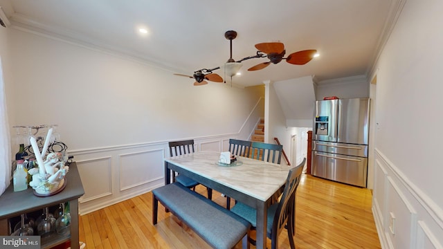 dining room featuring ceiling fan, stairway, ornamental molding, light wood-style floors, and a decorative wall