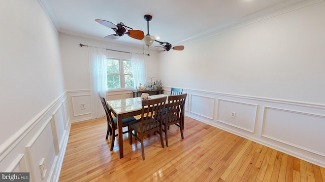 dining area with ornamental molding, light wood-style floors, a decorative wall, and a ceiling fan