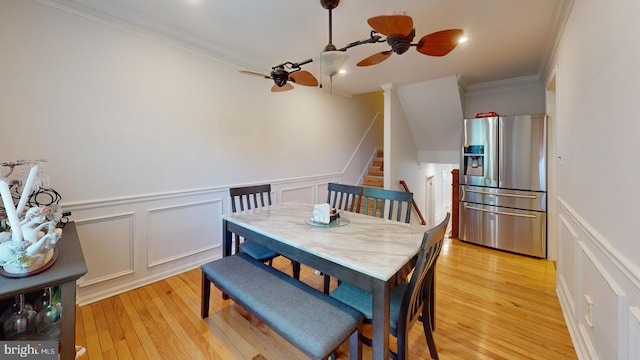 dining room with a decorative wall, a ceiling fan, stairs, ornamental molding, and light wood-type flooring