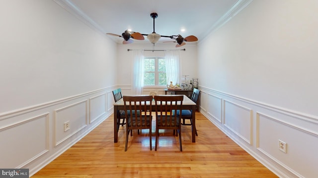 dining space featuring ornamental molding, a decorative wall, and light wood-style flooring