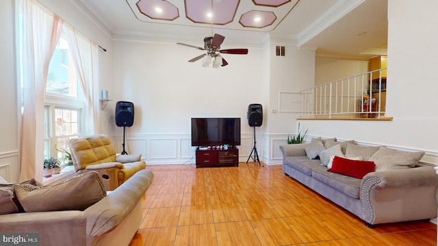 living area featuring visible vents, a decorative wall, ornamental molding, wainscoting, and ceiling fan