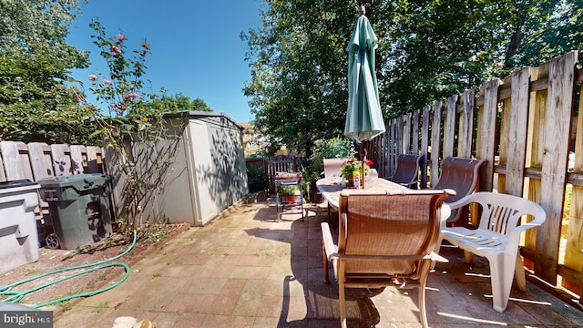 view of patio / terrace with an outbuilding, a shed, outdoor dining space, and a fenced backyard