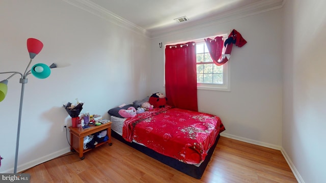 bedroom with crown molding, visible vents, baseboards, and wood finished floors