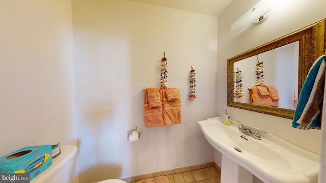 half bath with baseboards, a sink, and toilet