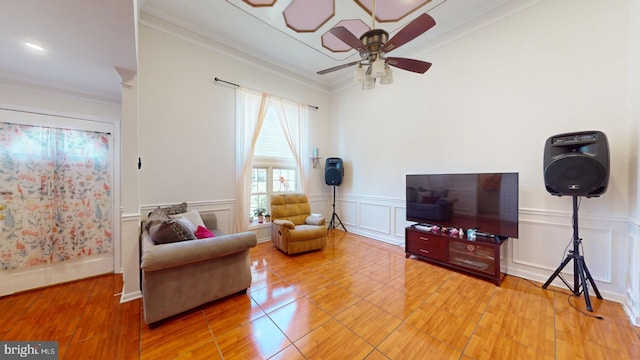 living area featuring ornamental molding, wainscoting, a decorative wall, and ceiling fan