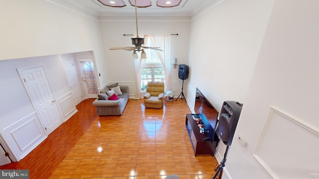 living room featuring light wood finished floors, a towering ceiling, ceiling fan, ornamental molding, and a decorative wall