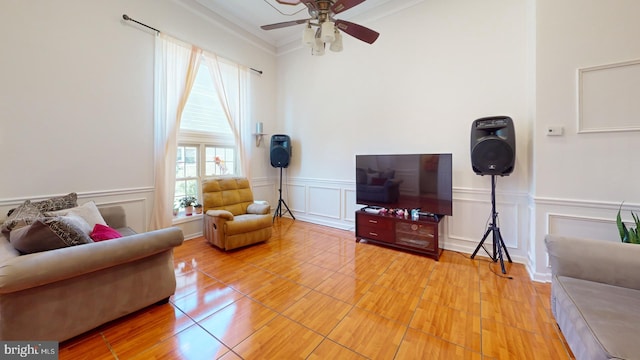 living area with a ceiling fan, a decorative wall, and ornamental molding