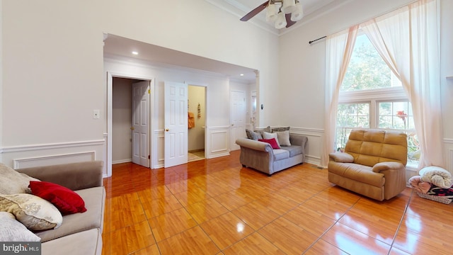 living room featuring a decorative wall, a high ceiling, wood finished floors, ornamental molding, and wainscoting