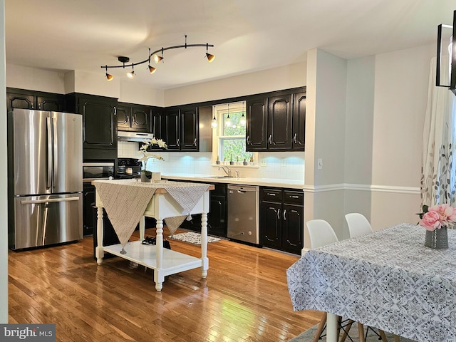 kitchen featuring rail lighting, decorative backsplash, wood-type flooring, and stainless steel appliances