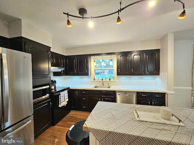 kitchen with appliances with stainless steel finishes, rail lighting, sink, light wood-type flooring, and exhaust hood