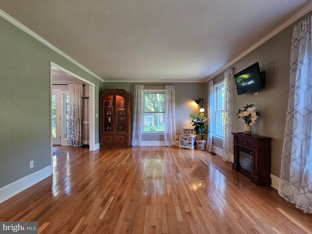 unfurnished living room featuring crown molding, a glass covered fireplace, wood finished floors, and baseboards