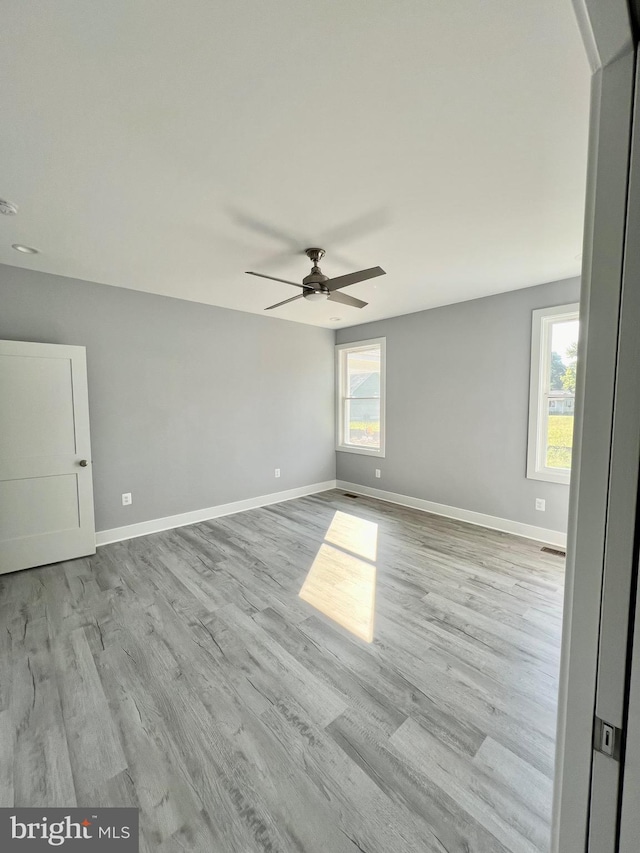 spare room featuring visible vents, light wood-type flooring, a ceiling fan, and baseboards