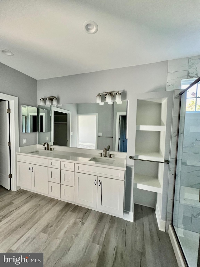 bathroom featuring double vanity, wood finished floors, a stall shower, and a sink