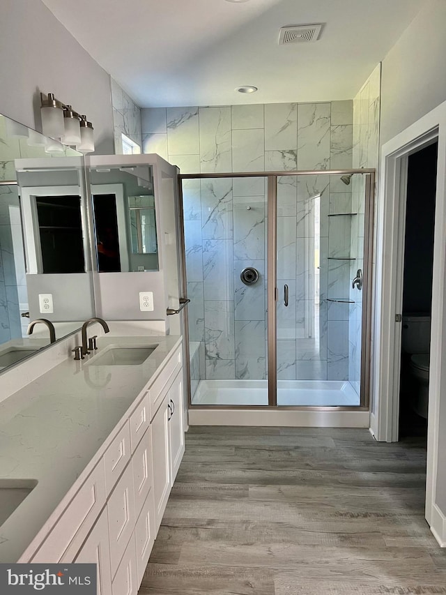 bathroom with a sink, wood finished floors, visible vents, a marble finish shower, and double vanity