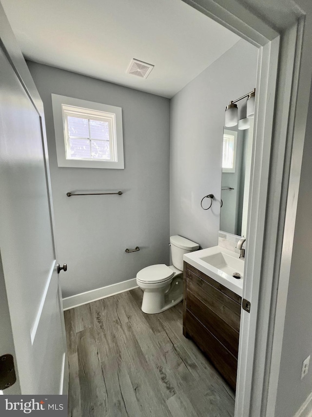 half bathroom featuring toilet, wood finished floors, vanity, visible vents, and baseboards