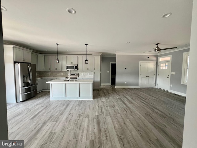 kitchen featuring a kitchen island with sink, gray cabinetry, open floor plan, light countertops, and appliances with stainless steel finishes