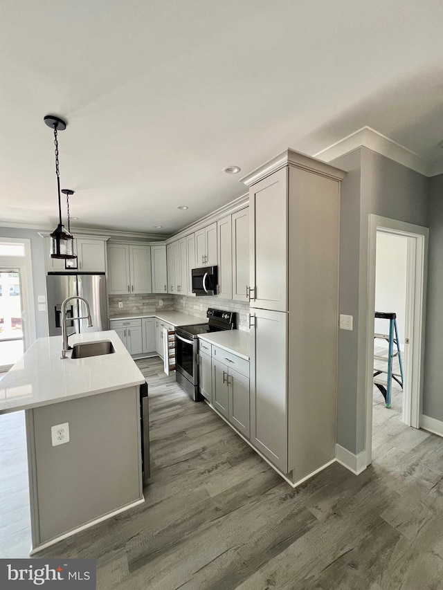 kitchen featuring light countertops, appliances with stainless steel finishes, a kitchen island with sink, a sink, and wood finished floors