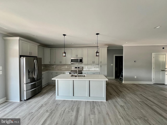 kitchen featuring appliances with stainless steel finishes, hanging light fixtures, a kitchen island with sink, gray cabinets, and light countertops