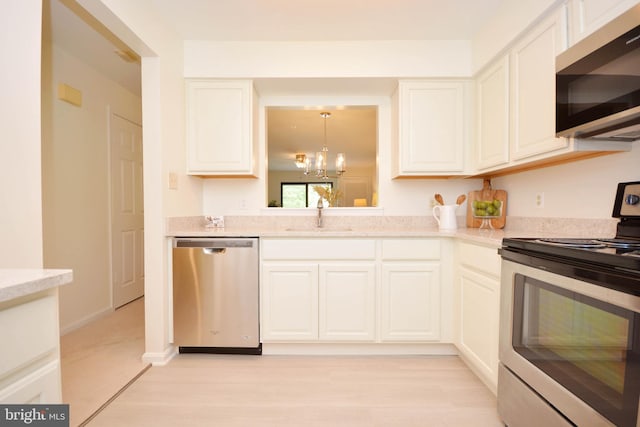 kitchen featuring sink, appliances with stainless steel finishes, a notable chandelier, white cabinets, and decorative light fixtures