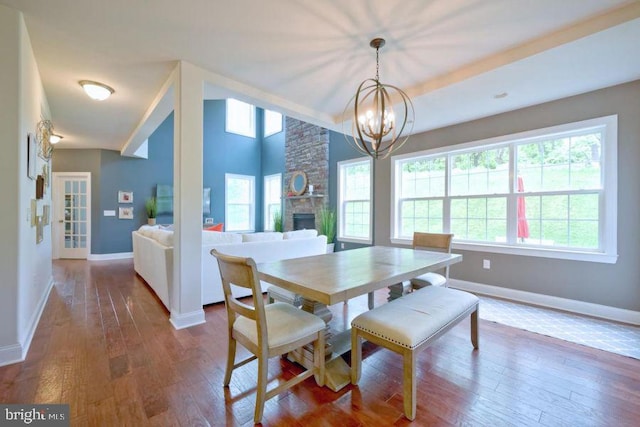 dining room with a stone fireplace, hardwood / wood-style floors, and a notable chandelier