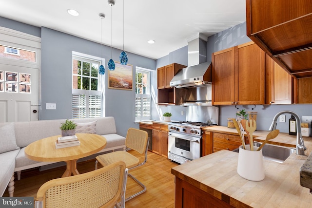 kitchen featuring pendant lighting, sink, high end stainless steel range, light hardwood / wood-style floors, and wall chimney range hood