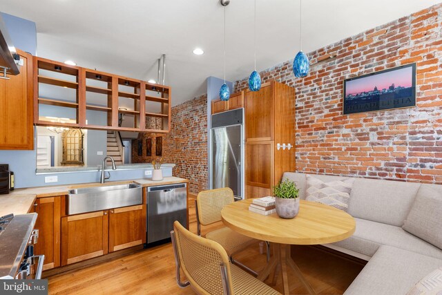 kitchen featuring sink, stainless steel appliances, brick wall, decorative light fixtures, and light wood-type flooring