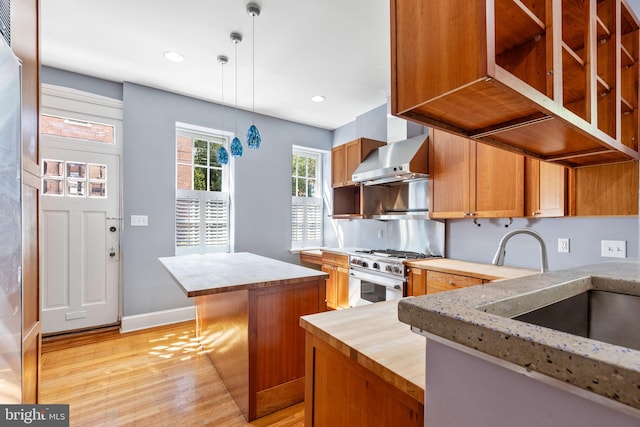 kitchen with a kitchen island, extractor fan, stainless steel range, decorative light fixtures, and light hardwood / wood-style floors