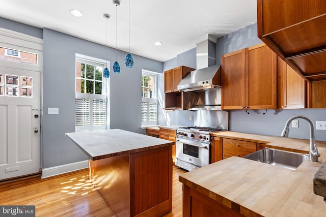 kitchen featuring wall chimney range hood, sink, a center island, hanging light fixtures, and high end stove