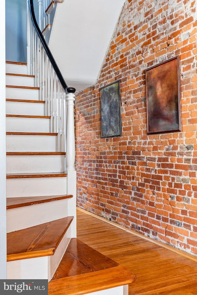 stairs with brick wall, lofted ceiling, and hardwood / wood-style floors