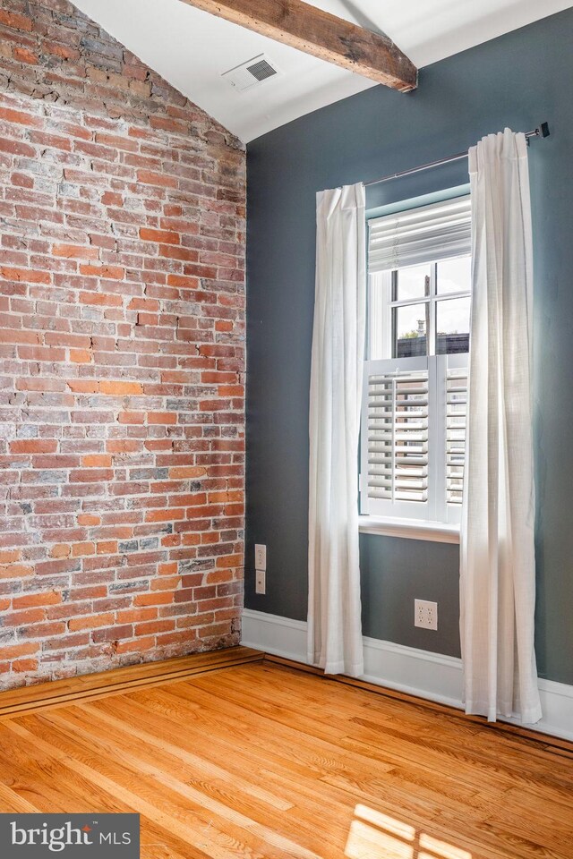 unfurnished room featuring french doors, hardwood / wood-style flooring, lofted ceiling with beams, and brick wall