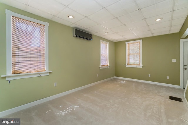 carpeted empty room with a drop ceiling, a wall mounted air conditioner, and a healthy amount of sunlight