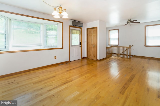 interior space with ceiling fan with notable chandelier, an AC wall unit, and light hardwood / wood-style floors