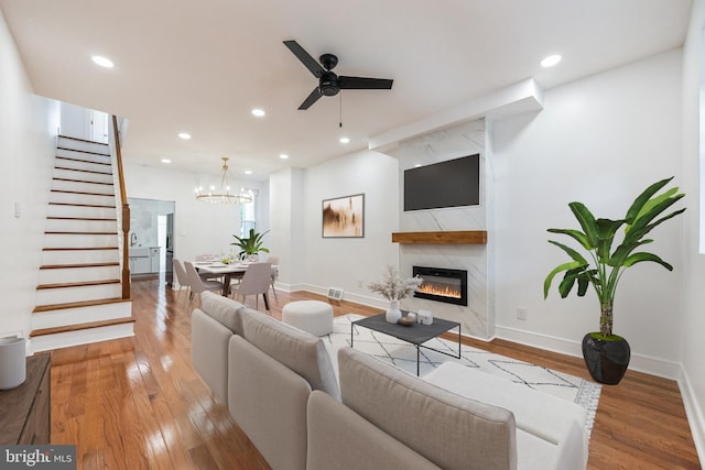 living room featuring sink, ceiling fan with notable chandelier, a fireplace, and light hardwood / wood-style flooring