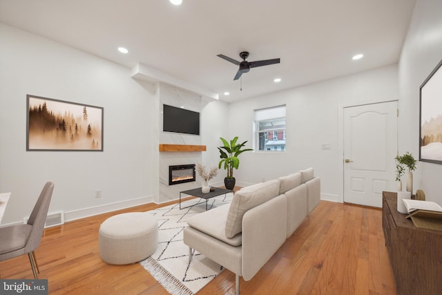 living room with ceiling fan, a fireplace, and light hardwood / wood-style flooring