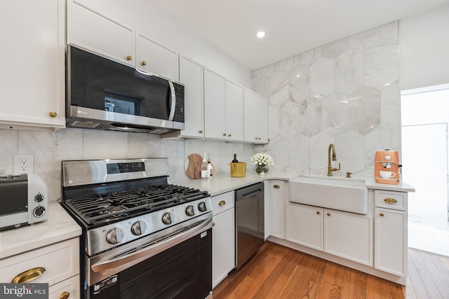 kitchen featuring white cabinetry, appliances with stainless steel finishes, backsplash, light wood-type flooring, and sink