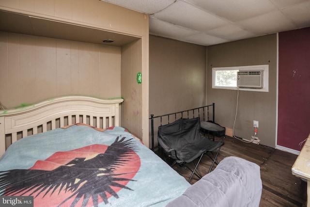 bedroom with dark wood-type flooring, a wall mounted AC, and a drop ceiling