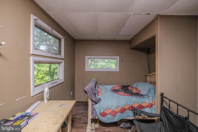 bedroom with wood walls, hardwood / wood-style floors, multiple windows, and a drop ceiling