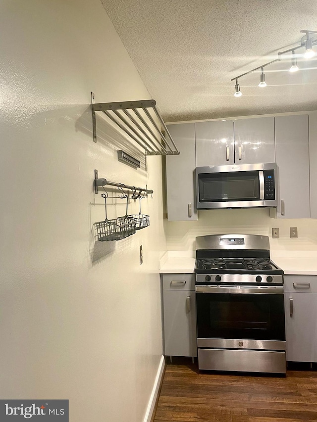 kitchen with a textured ceiling, rail lighting, appliances with stainless steel finishes, and dark hardwood / wood-style flooring