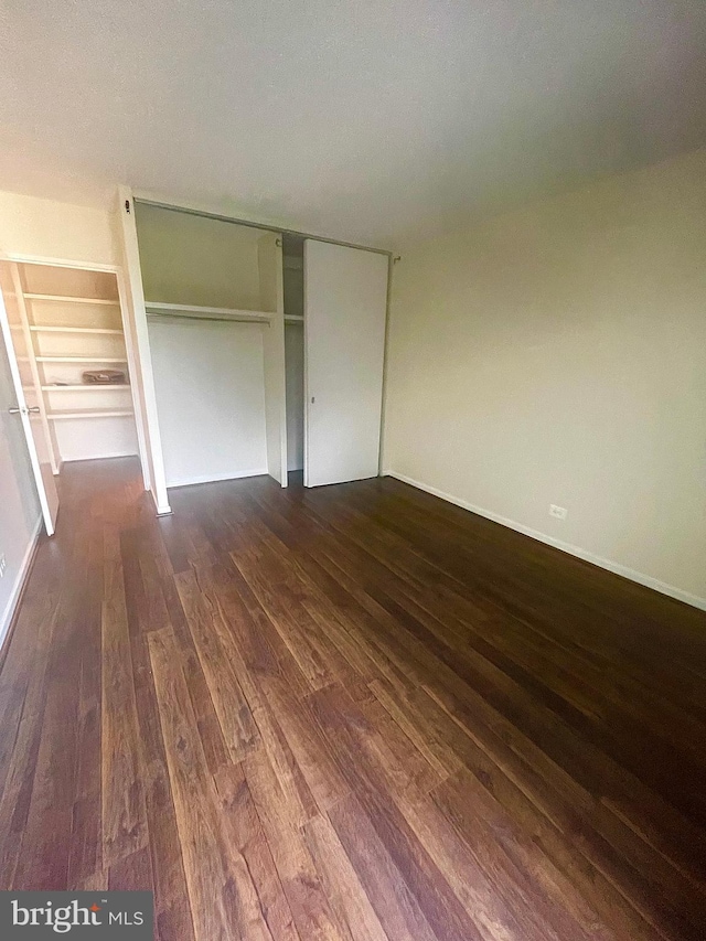 unfurnished bedroom featuring a textured ceiling, dark hardwood / wood-style flooring, and a closet